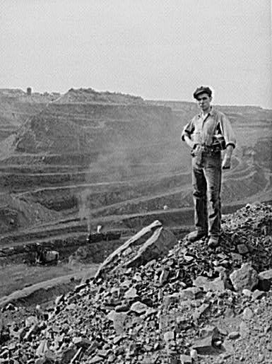 A miner poses near the edge of the pit. The pit is more than three miles (5 km) long, two miles (3 km) wide and 535 feet (163 m) deep.